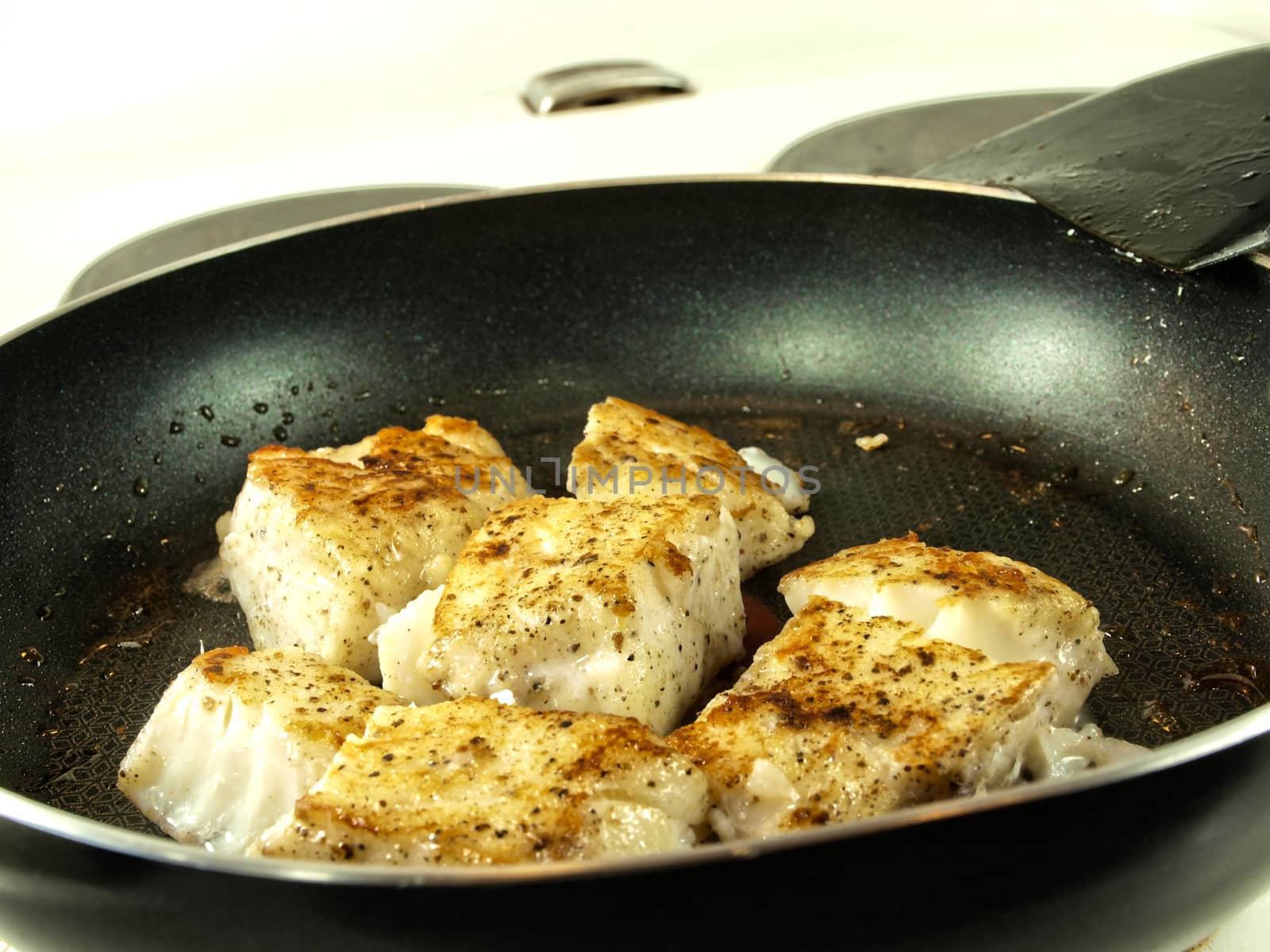 Someone frying seasoned white fish in a frying pan