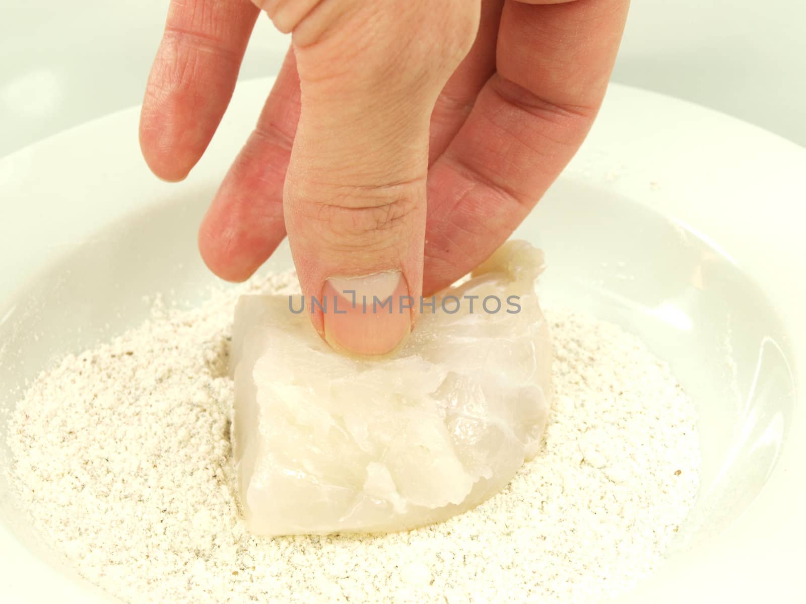 Person adding seasoning to a white fish fillet