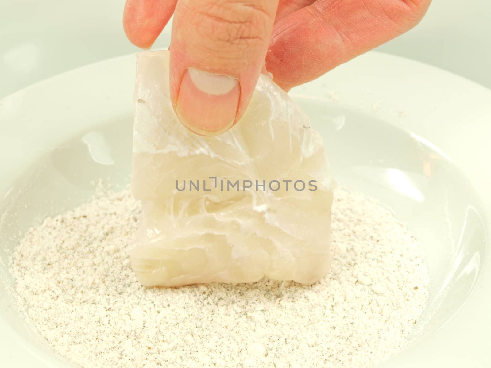 Person adding seasoning to a white fish fillet