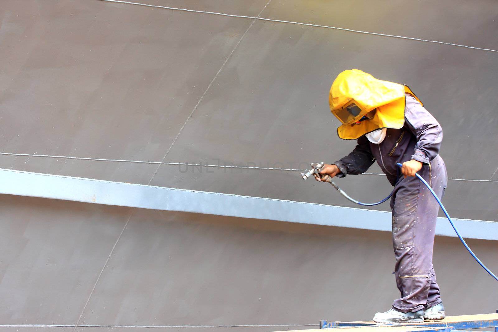 worker painting ship hull using airbrush