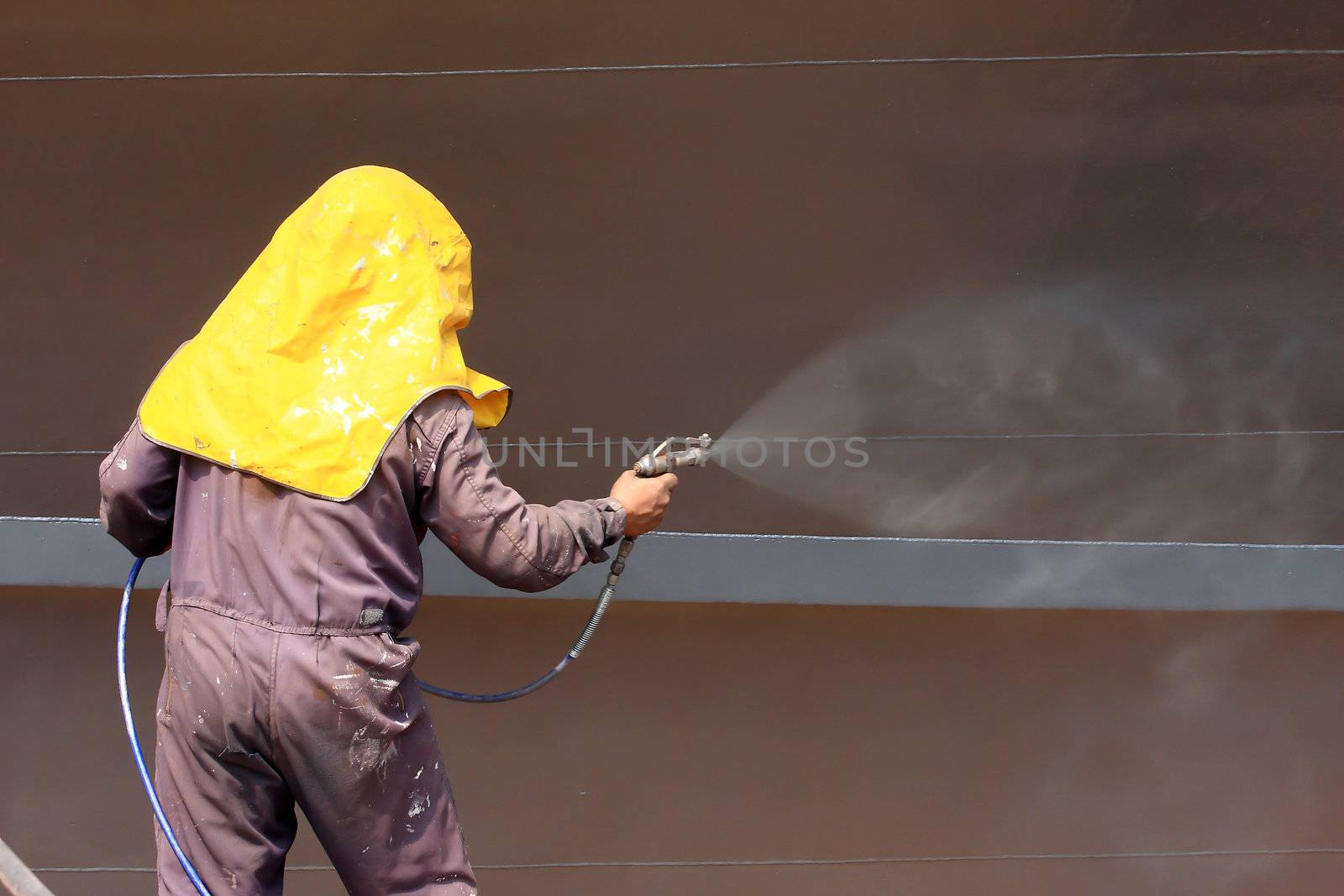 worker painting ship hull using airbrush