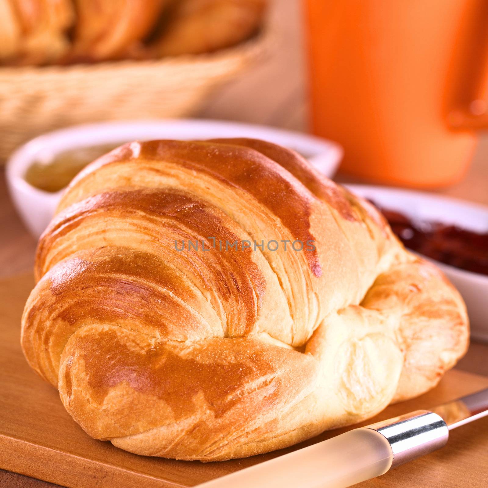 Croissant and jam for breakfast with cup in the back (Selective Focus, Focus one third into the croissant)