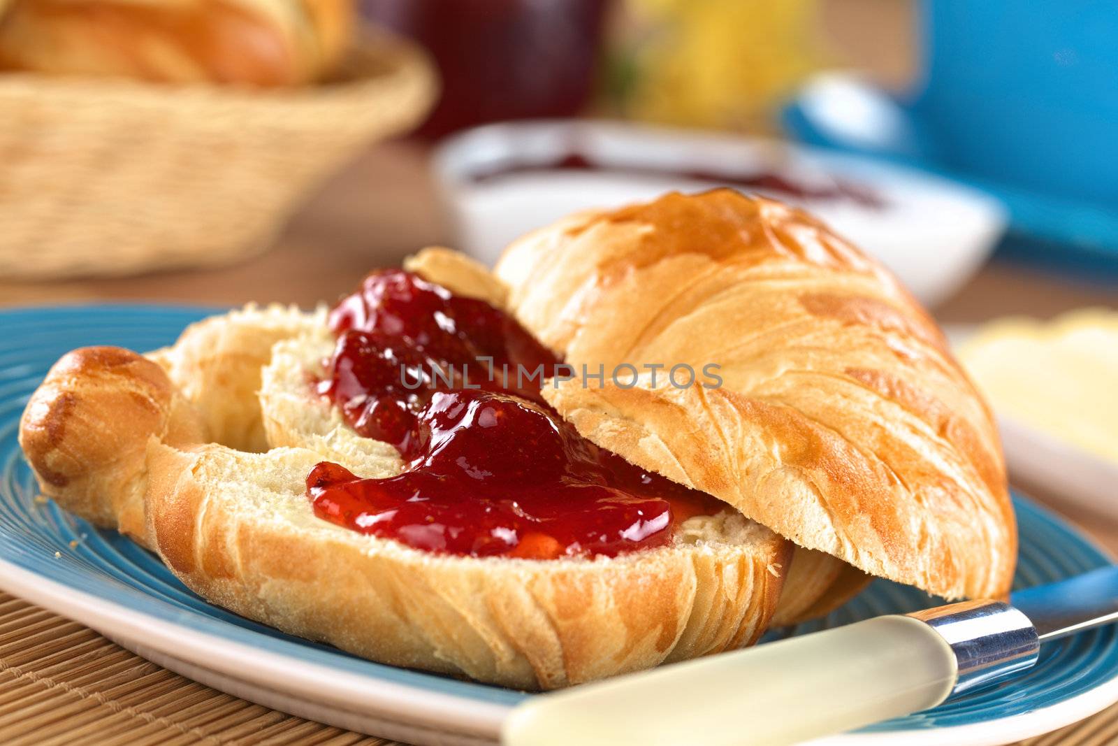 Croissant with butter and strawberry jam (Selective Focus, Focus on the front of the upper croissant half and the strawberry piece in the middle of the image)