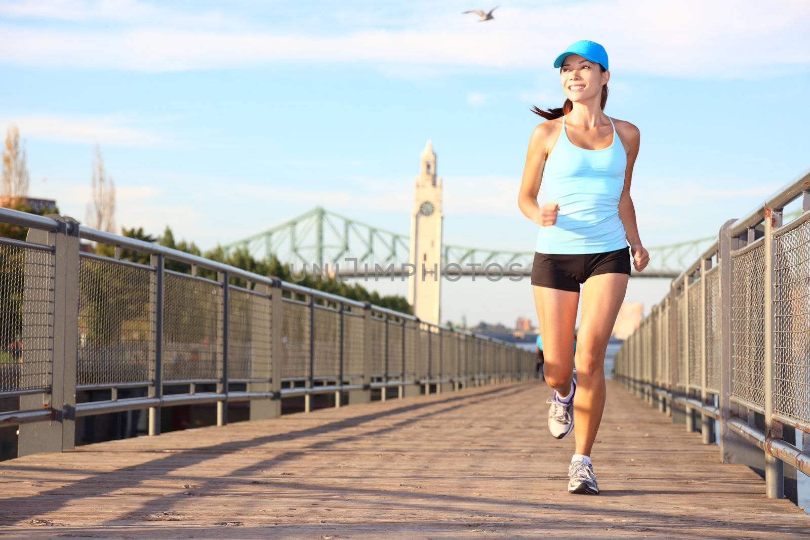 Running in city. Woman runner sport fitness model working out jogging smiling happy in Old Port of Montreal, Quebec, Canada. Beautiful young multiracial female runner.