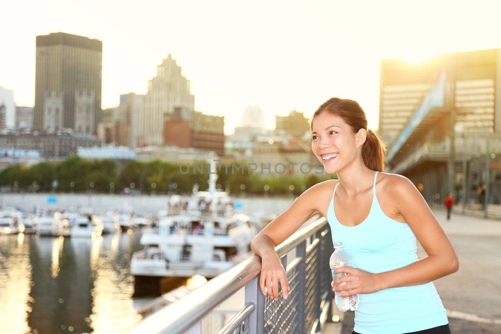 Woman city runner resting after running workout. Female fitness model smiling happy drinking water enjoying a break. Beautiful fit mixed race Asian Chinese and Caucasian woman outdoors.