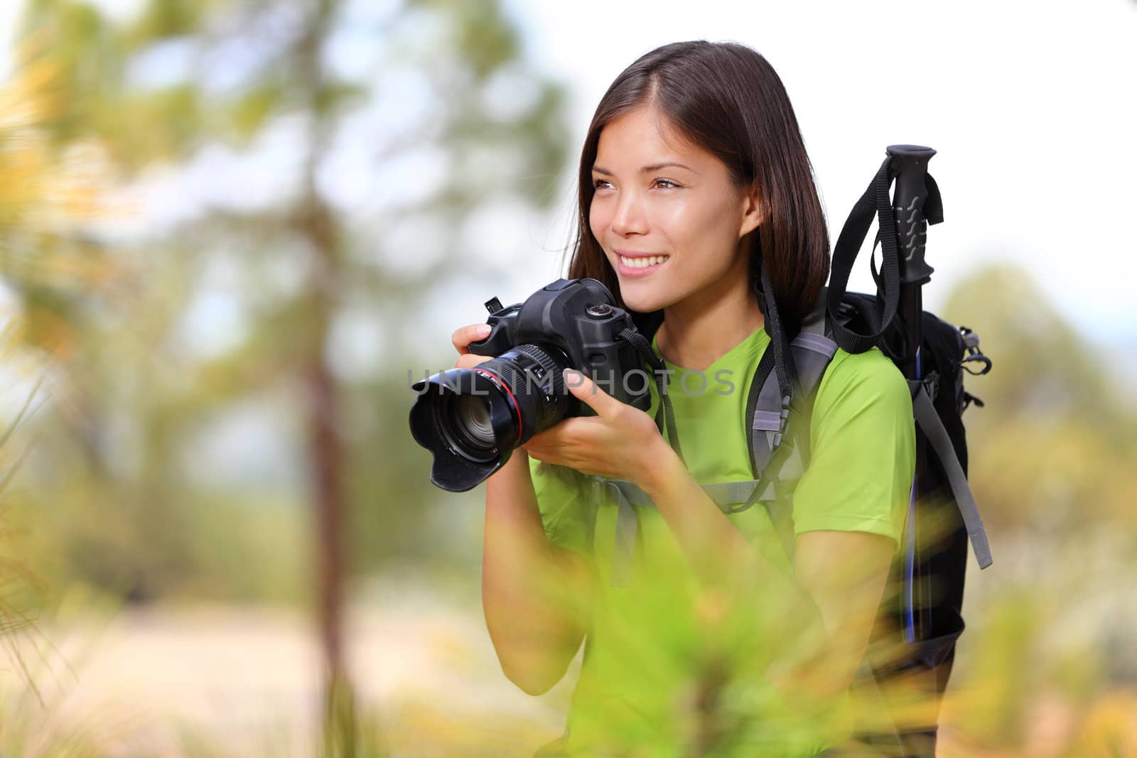 Nature travel photographer woman taking pictures in forest during hiking trip. Beautiful happy smiling young woman holding professional SLR camera. Mixed race Chinese Asian / Caucasian girl photographing