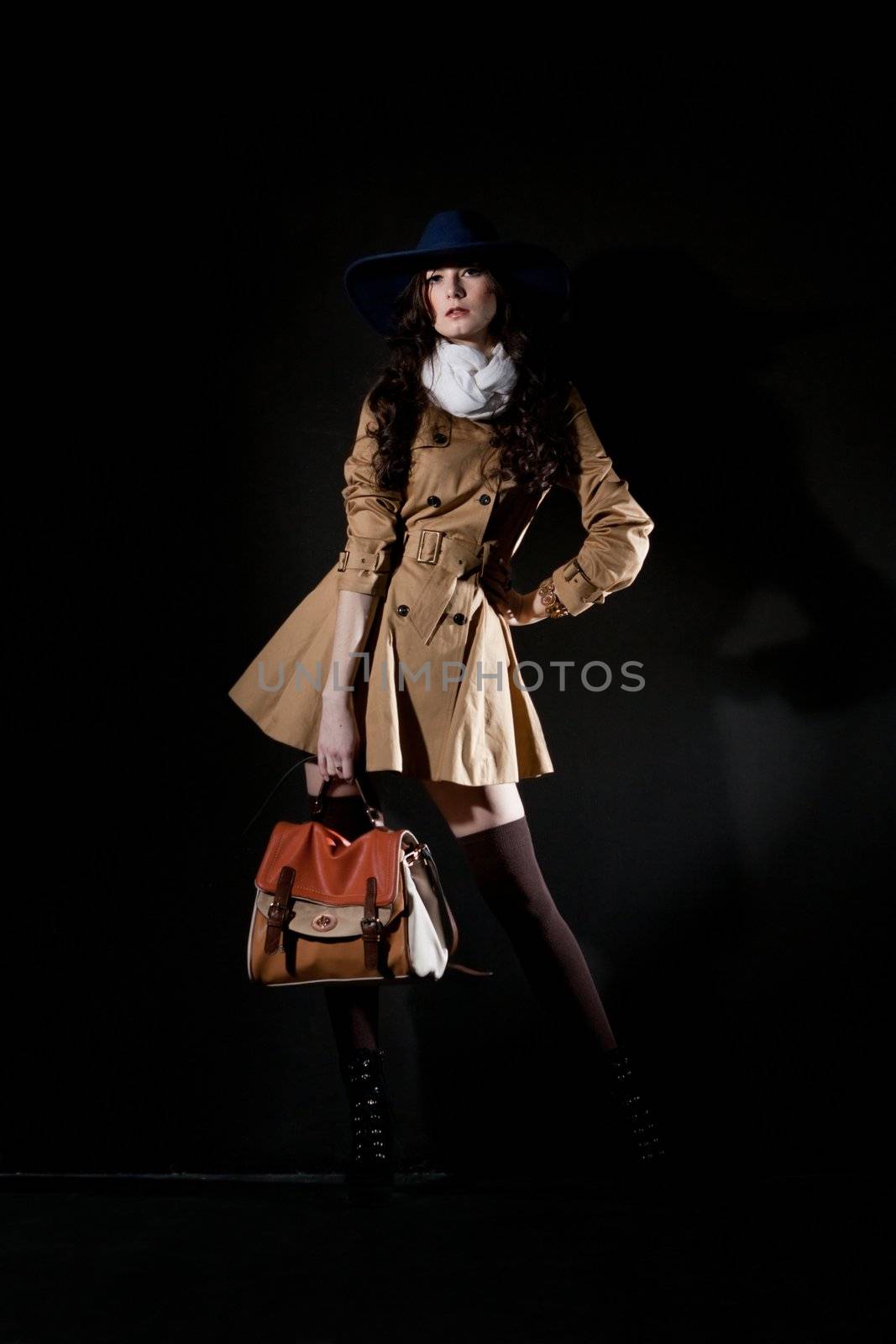 Expressive fashion studio shot of young and beautiful woman wearing brown overcoat on dark background. (Professional makeup and hair style).