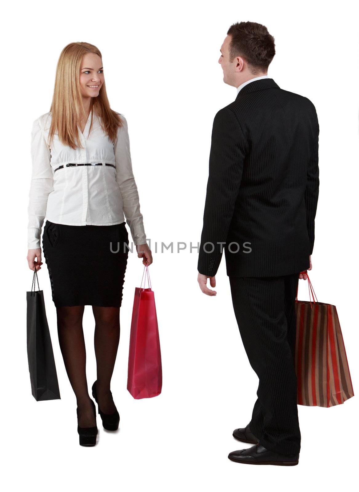 A man and a woman with shopping bags passing by themselves, against a white background.