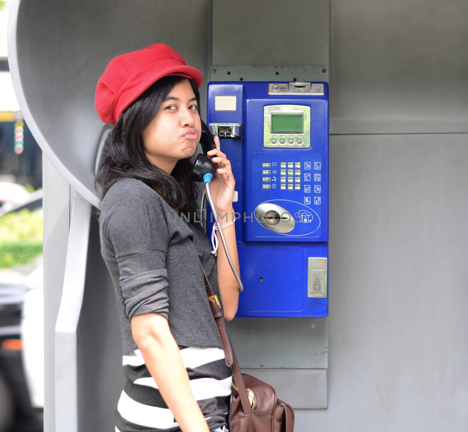 Hispanic woman talking in a public phone  by siraanamwong