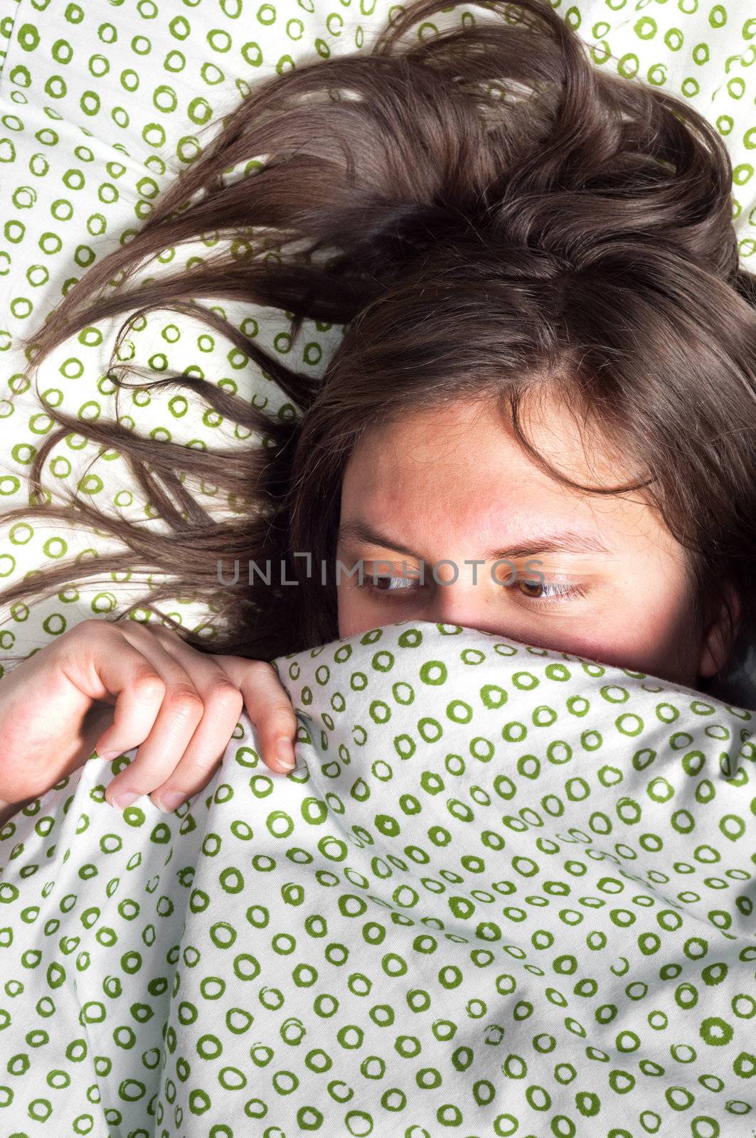 Young scared girl hiding under blanket