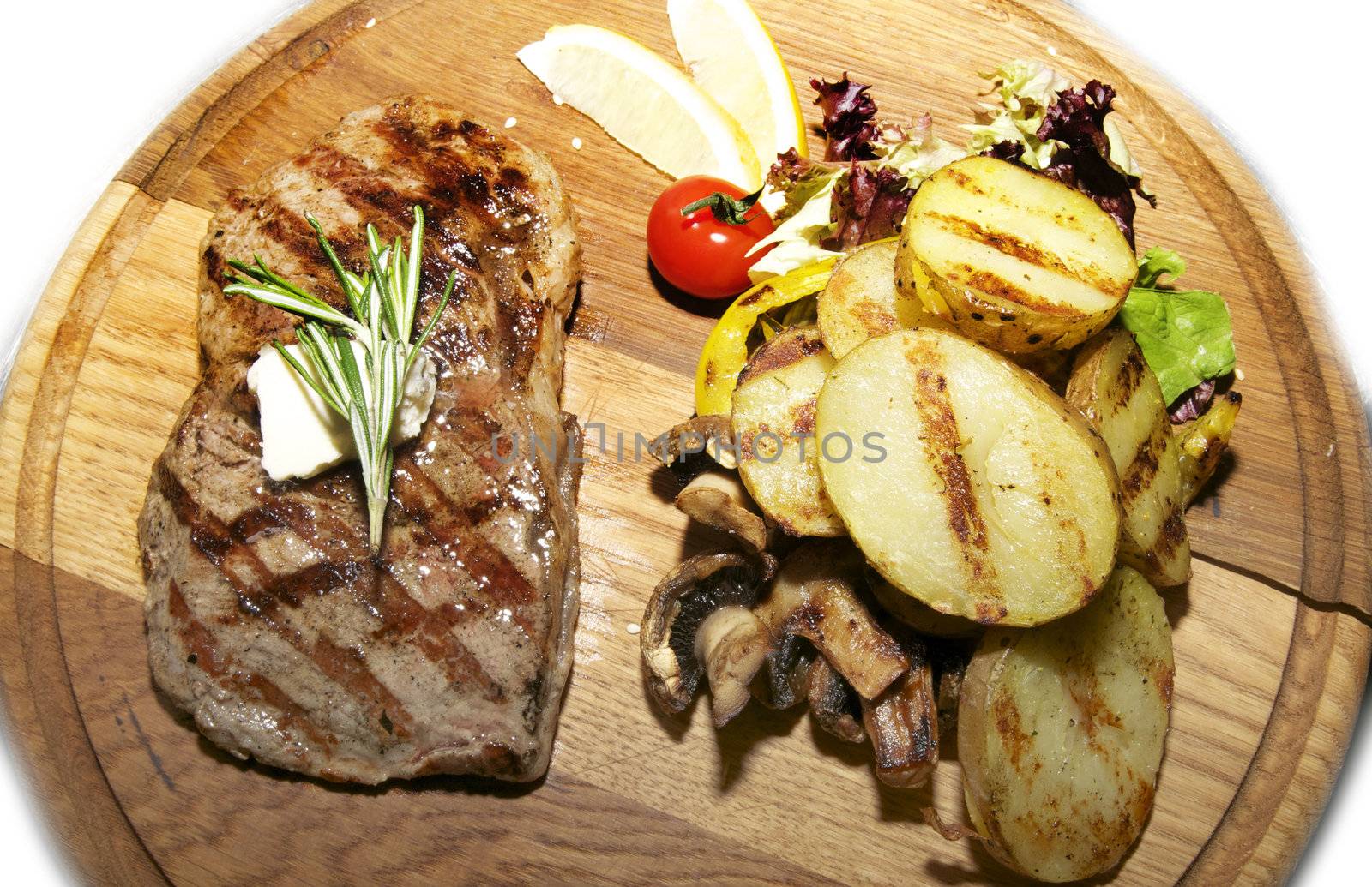 steak and potatoes on a large wooden plate with vegetables
