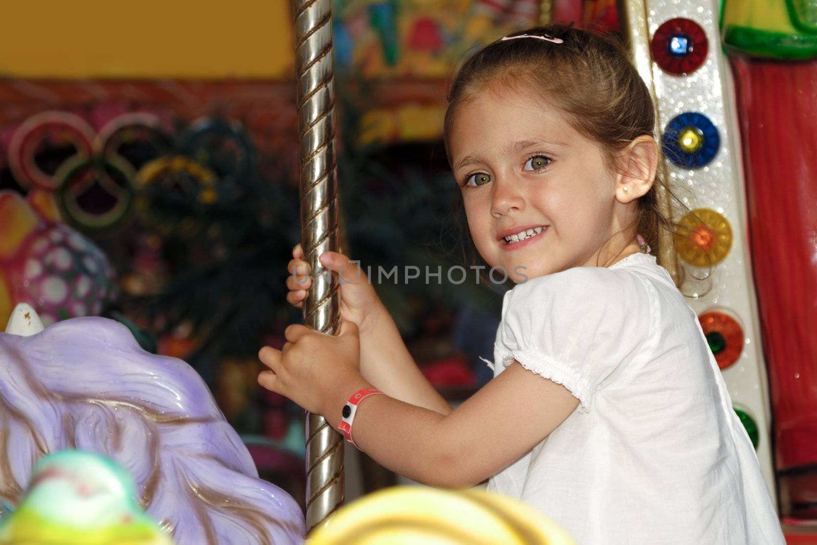 A sweet smiling child is sitting on horse in carousel
