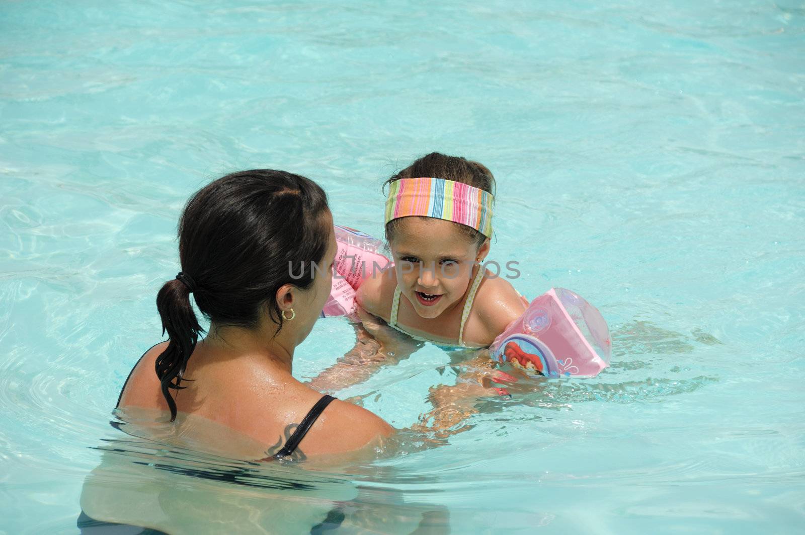 Child with mother is learning to swim in pool on vacation.