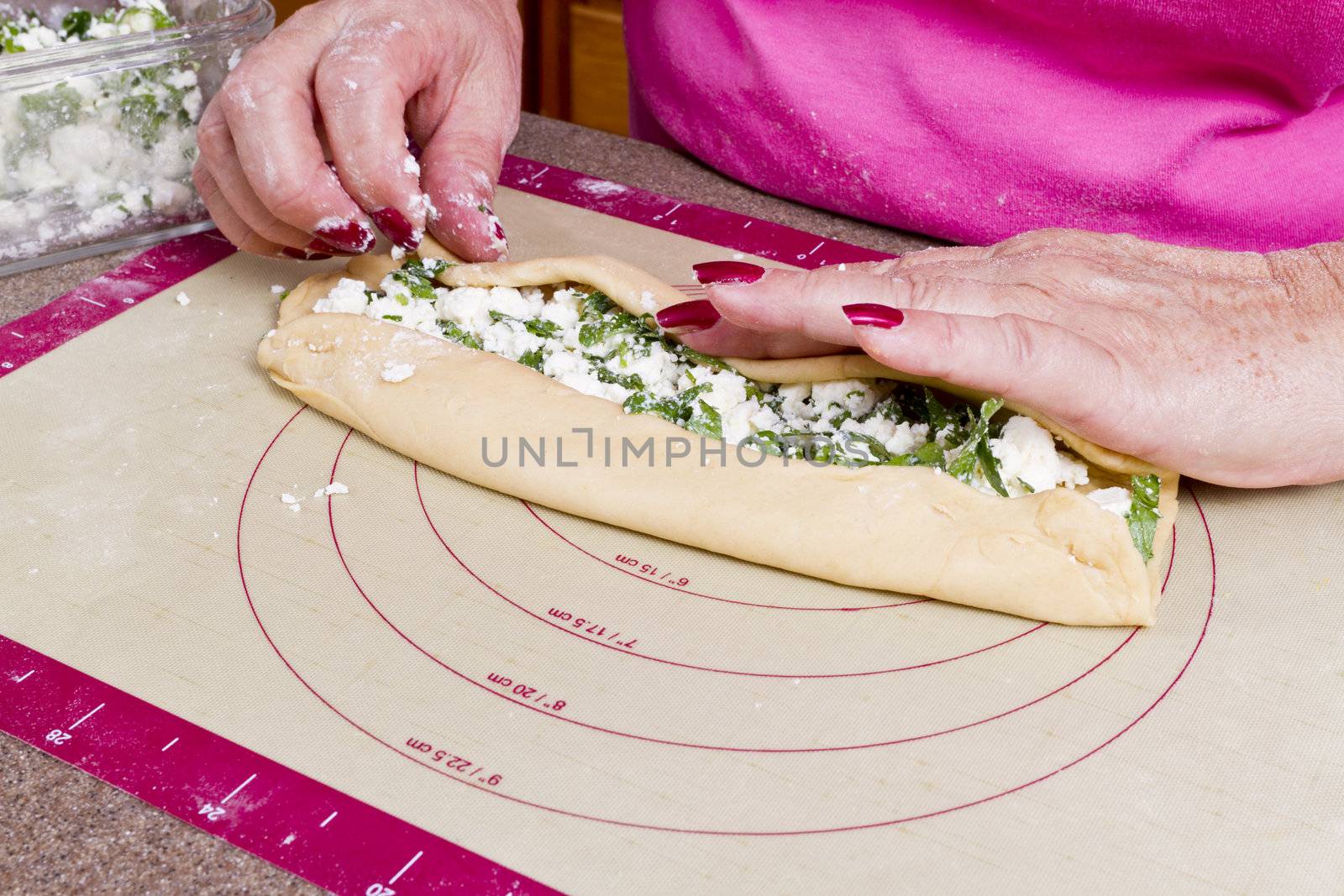 Older lady hands are wrapping Turkish feta cheese Pide pockets.