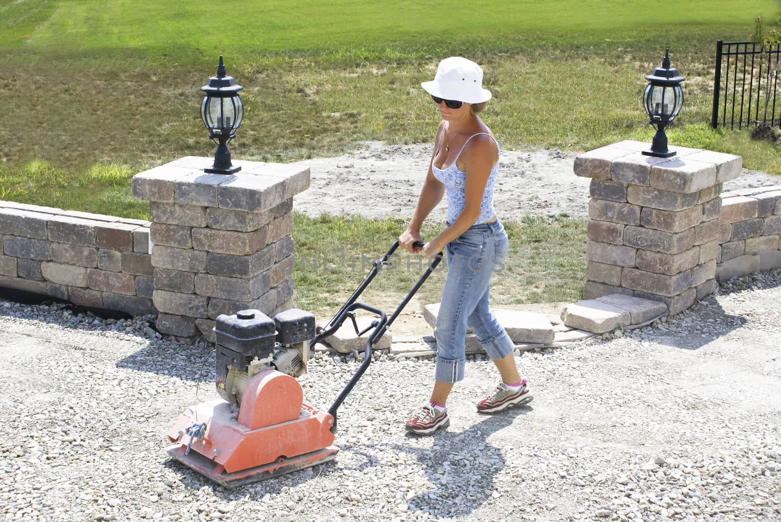 Woman with the white hat compacting patio base under the sun.
