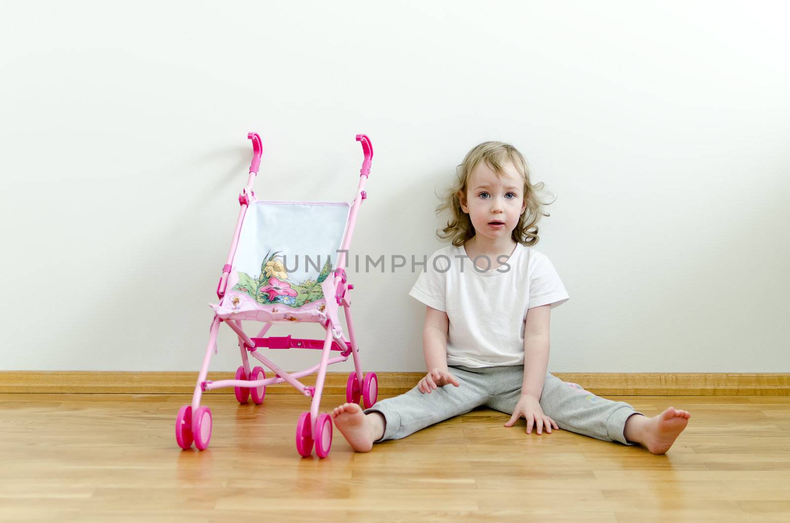 Little cute girl sitting on the floor next to the toy stroller