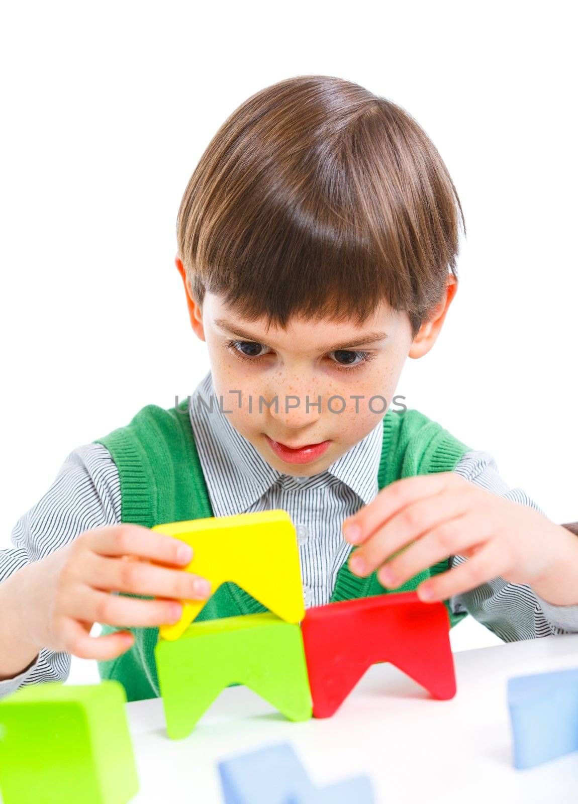 A smiling little boy is building a toy block. Isolated on white background