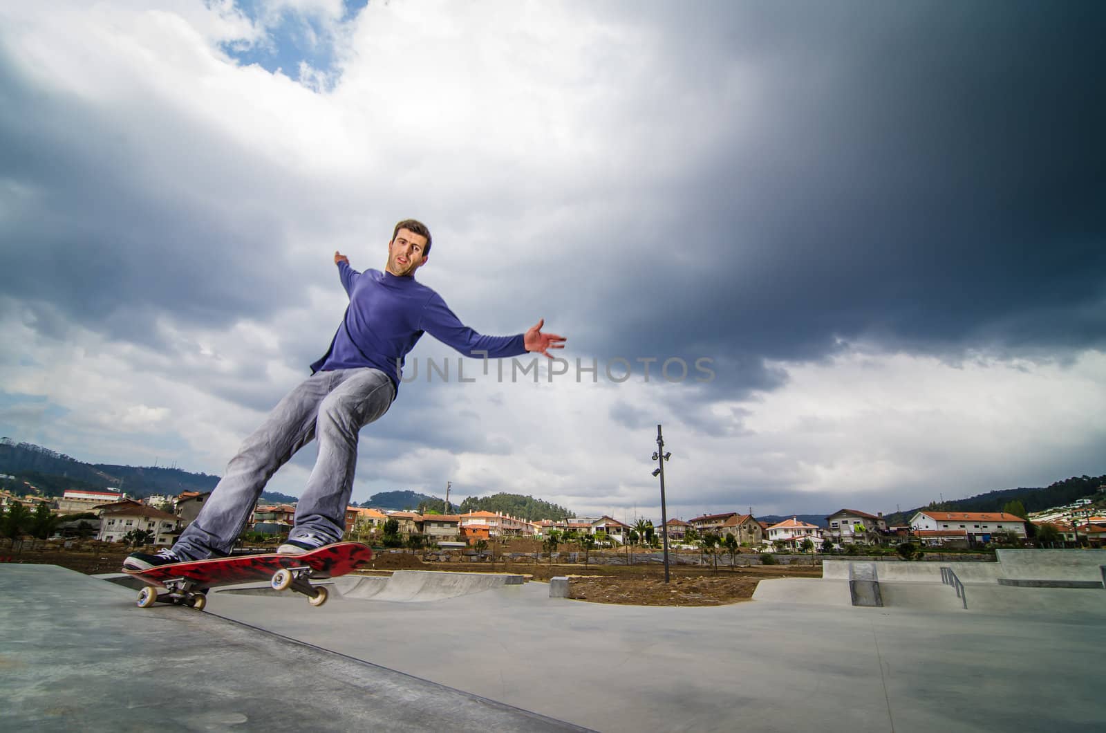 Skateboarder on a grind with dark clouds background at the local skatepark.