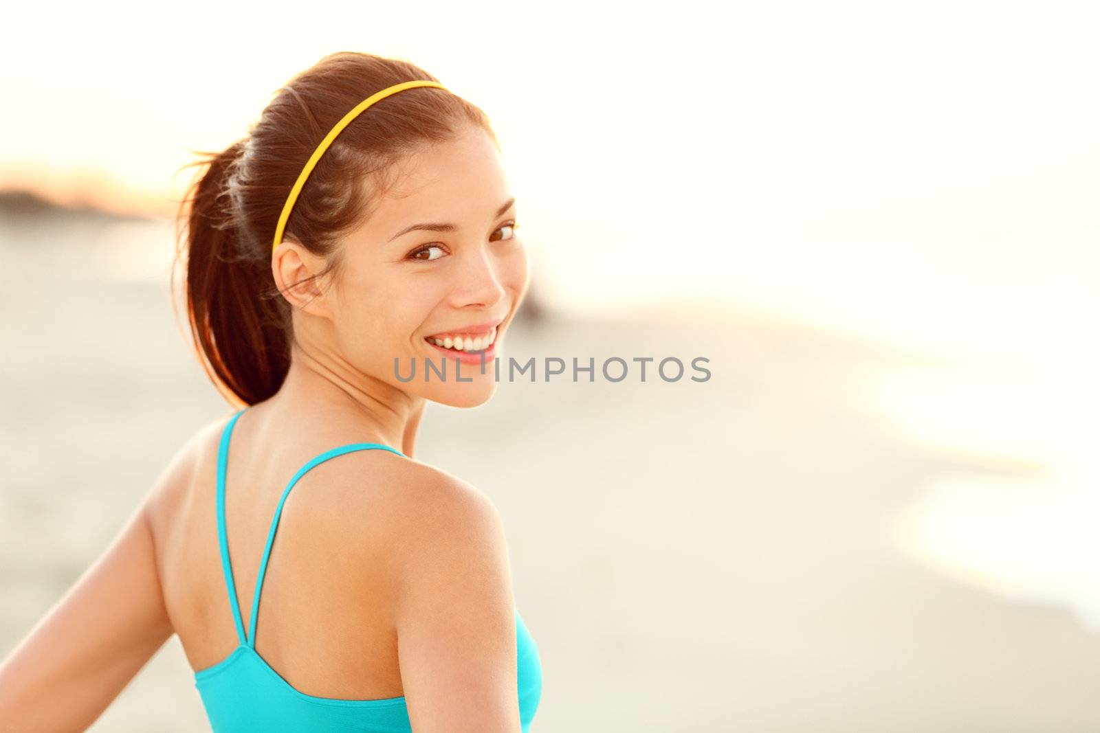 Fitness woman beach portrait. Happy sporty Asian runner resting and smiling after running workout outdoors on sunny summer day.