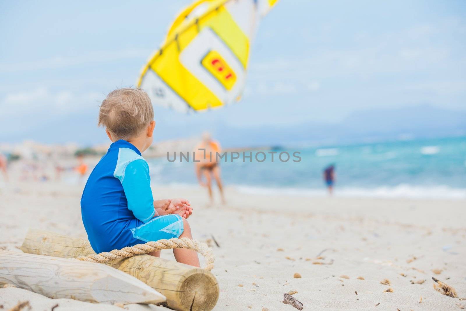 Back view cute 2 years old boy looking at kiting on tropical beach