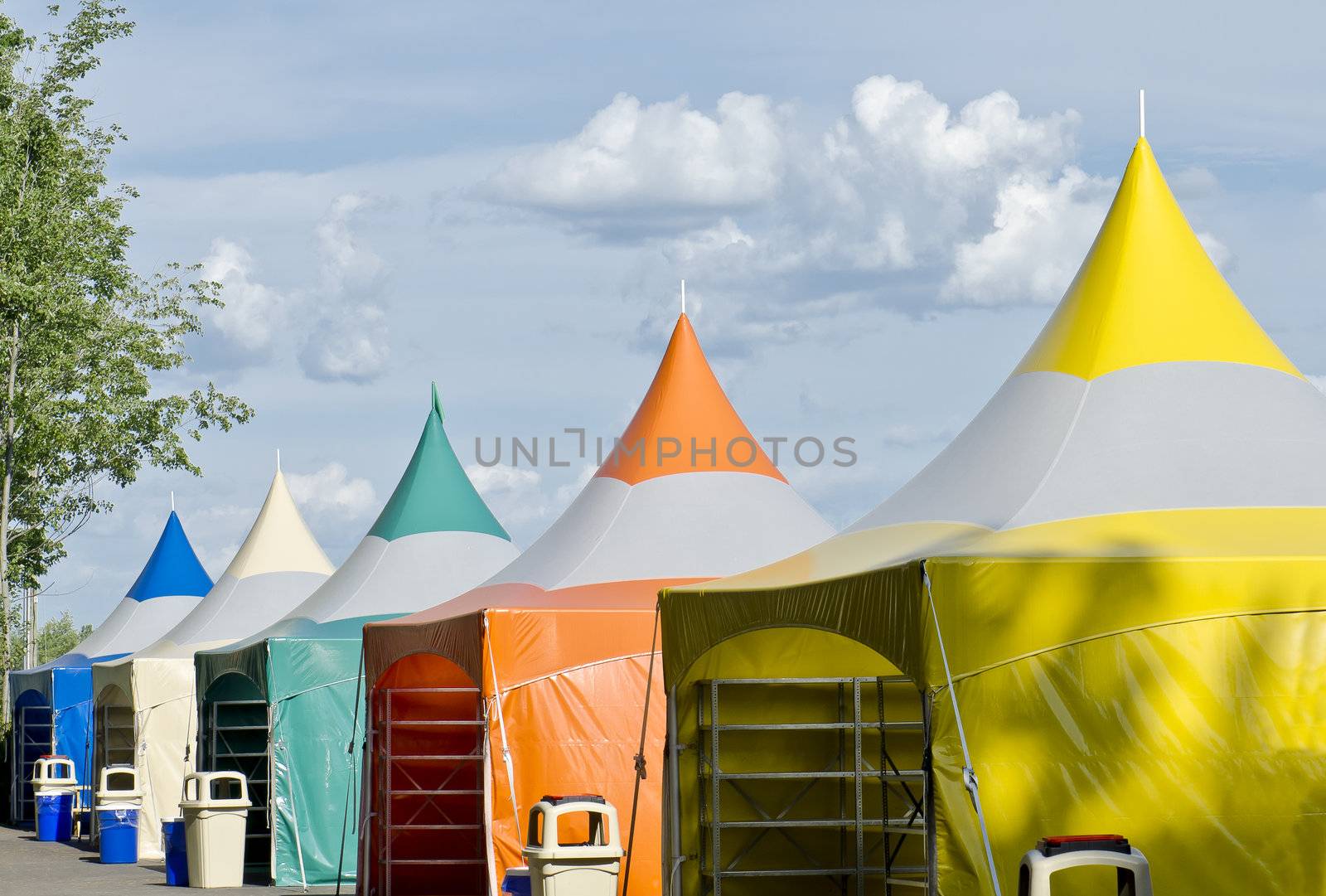 Five colorful carnival tents against a blue cloudy sky.