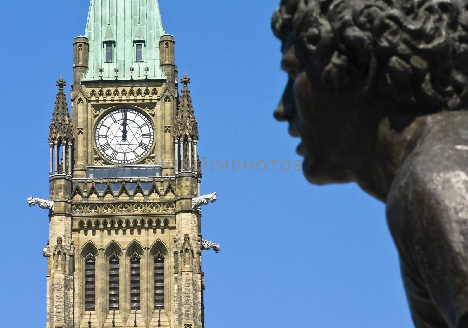 A statue of Terry Fox running in front of the canadian Parliament Centre Block at noon.