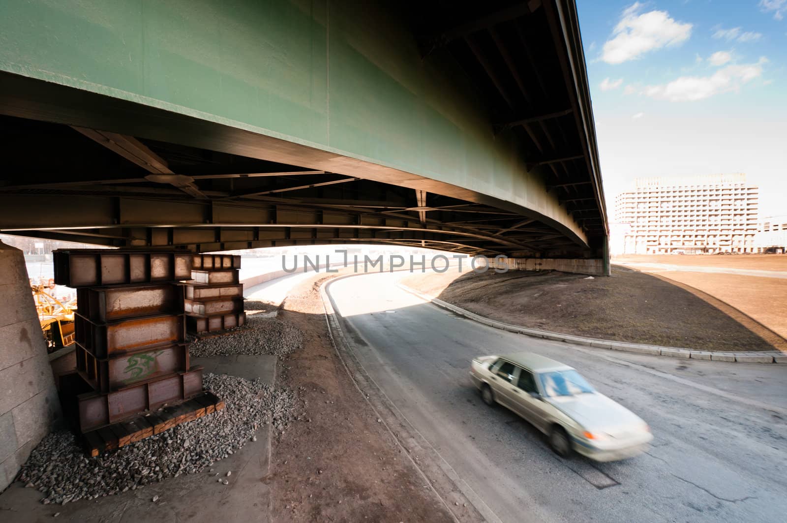 Blurred car moving under an old metal and green bridge