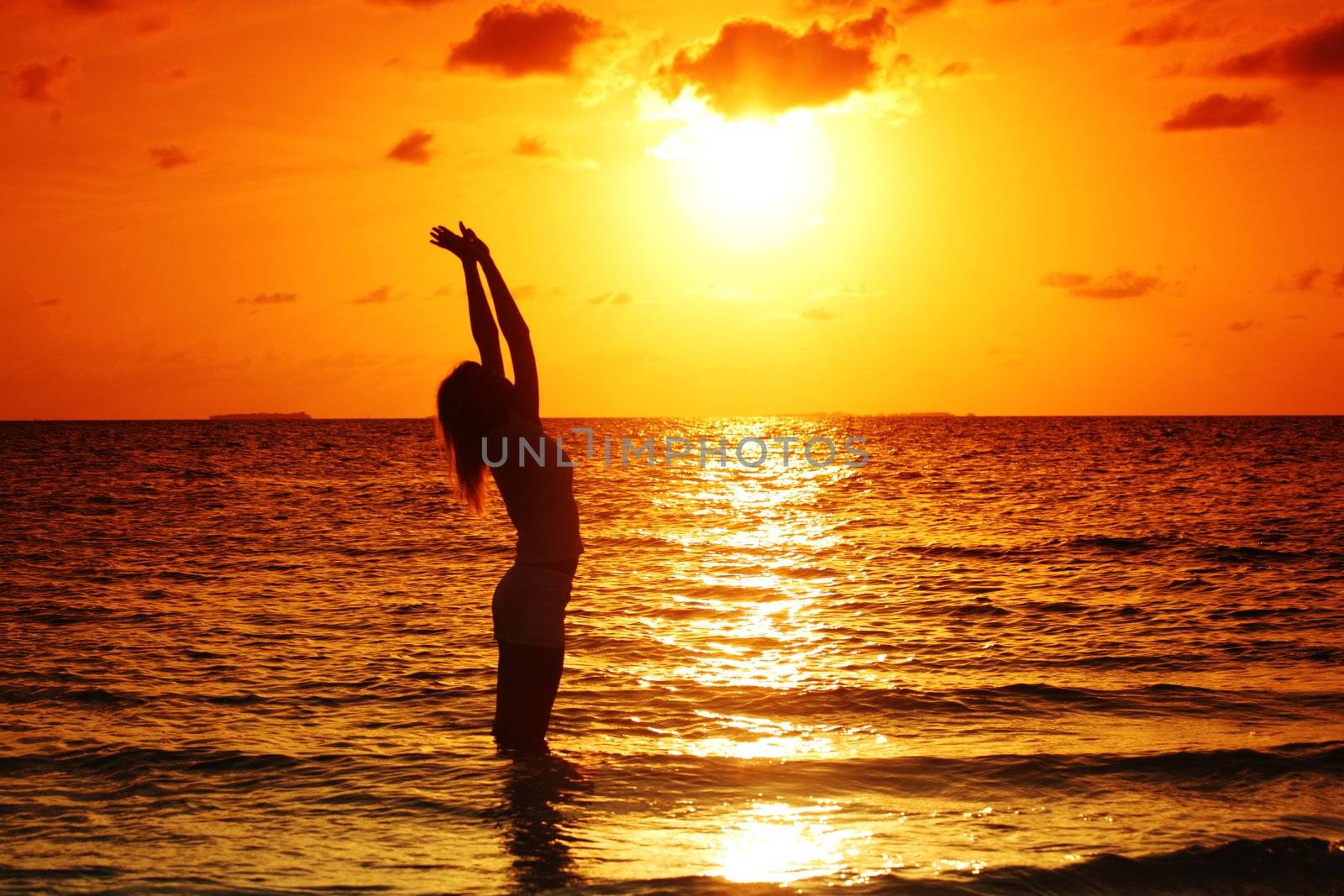 happy woman standing on a sunset in ocean waves