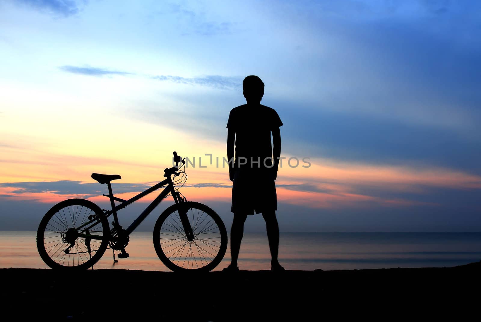 Silhouette of man riding bicycle with beautiful lake near by at sunset