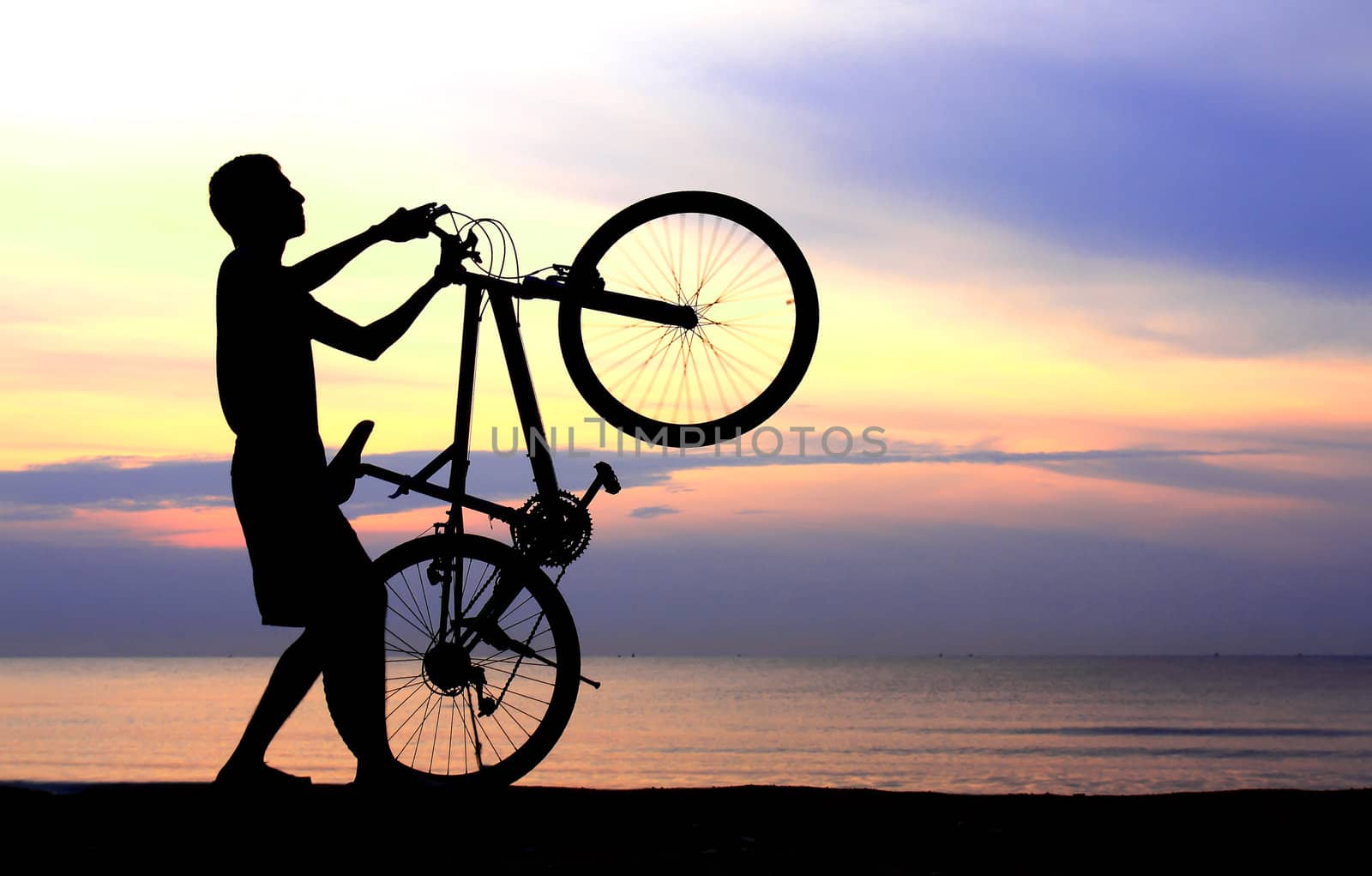 Silhouette of man riding bicycle with beautiful lake near by at sunset