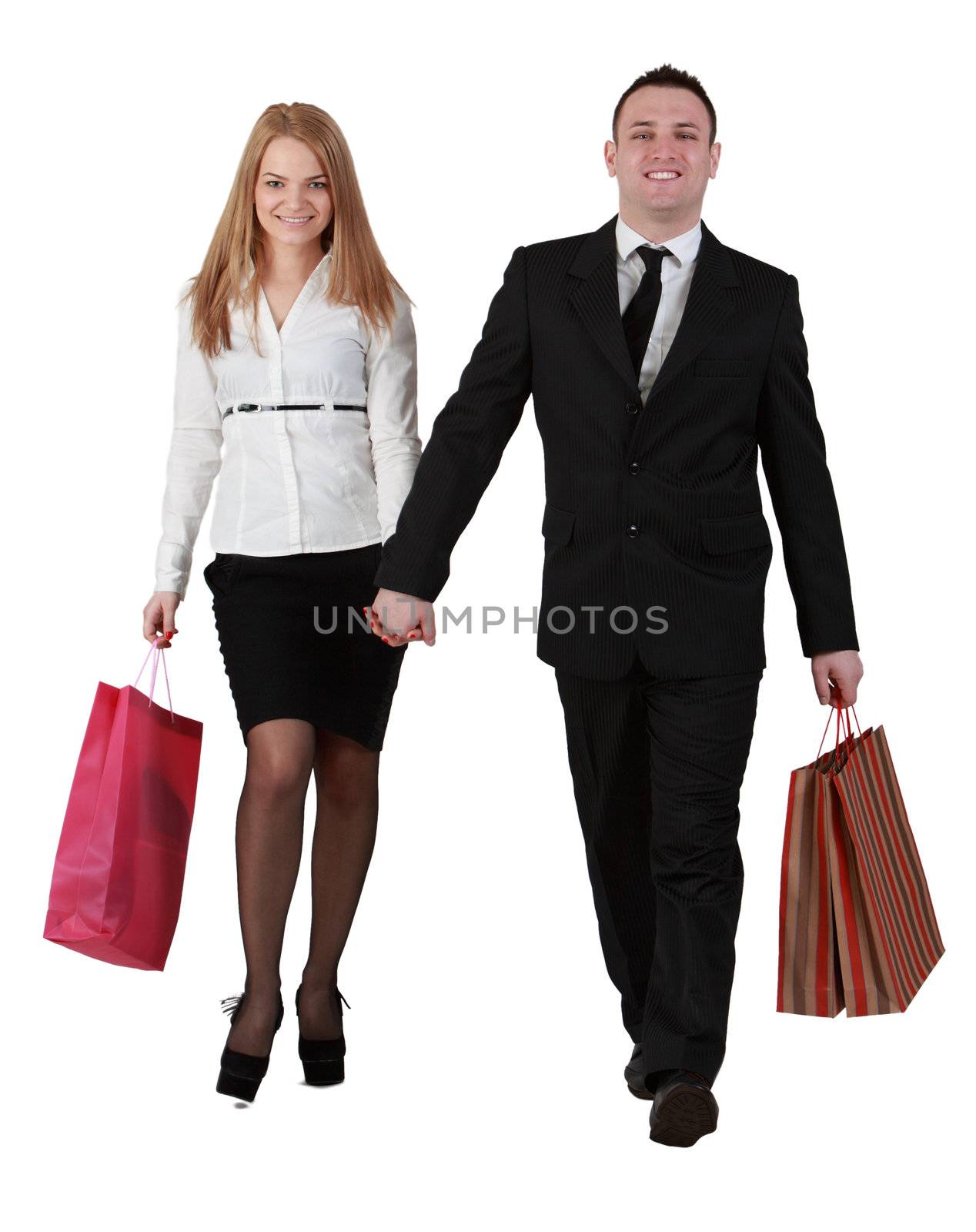 Happy young couple carrying shopping bags and holding their hands, coming through the camera, against a white background.