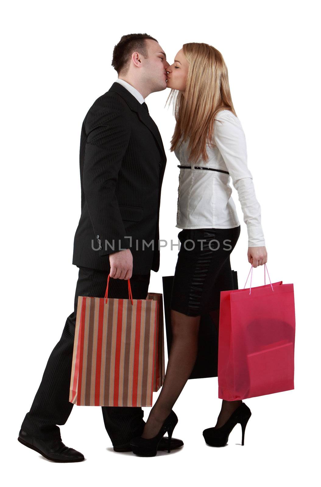 Young couple holding shopping bags and kissing against a white background.