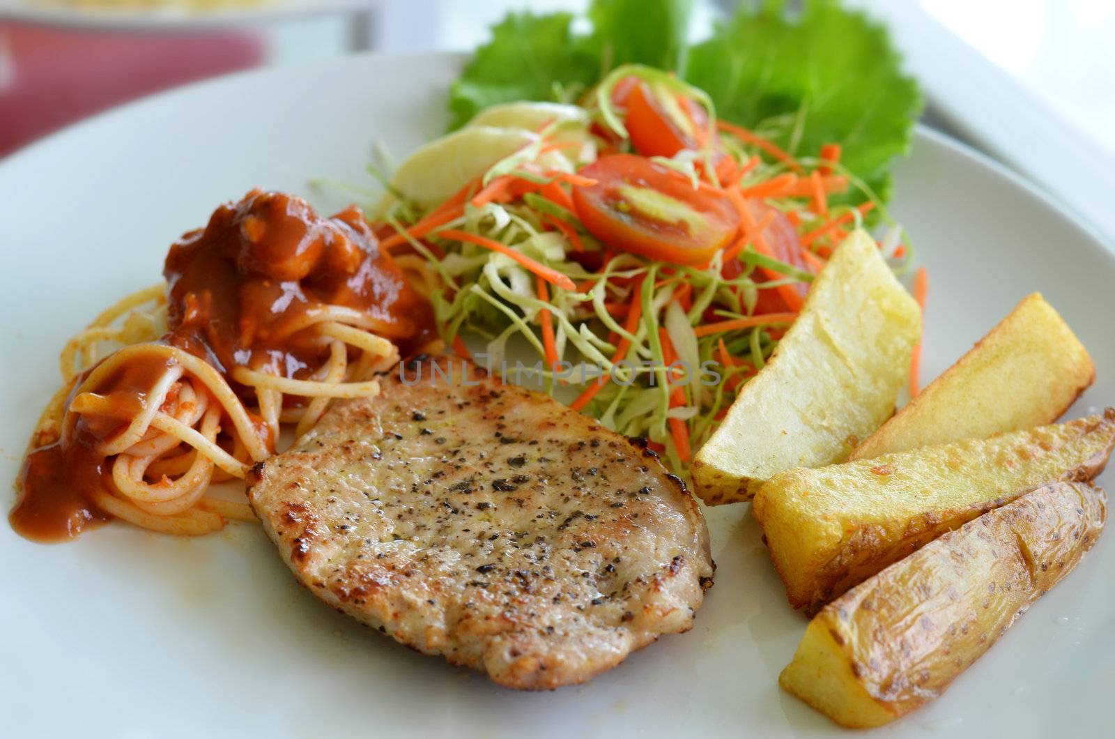 Grilled pork steak served with chips, potatoes and vegetables , spaghetti .