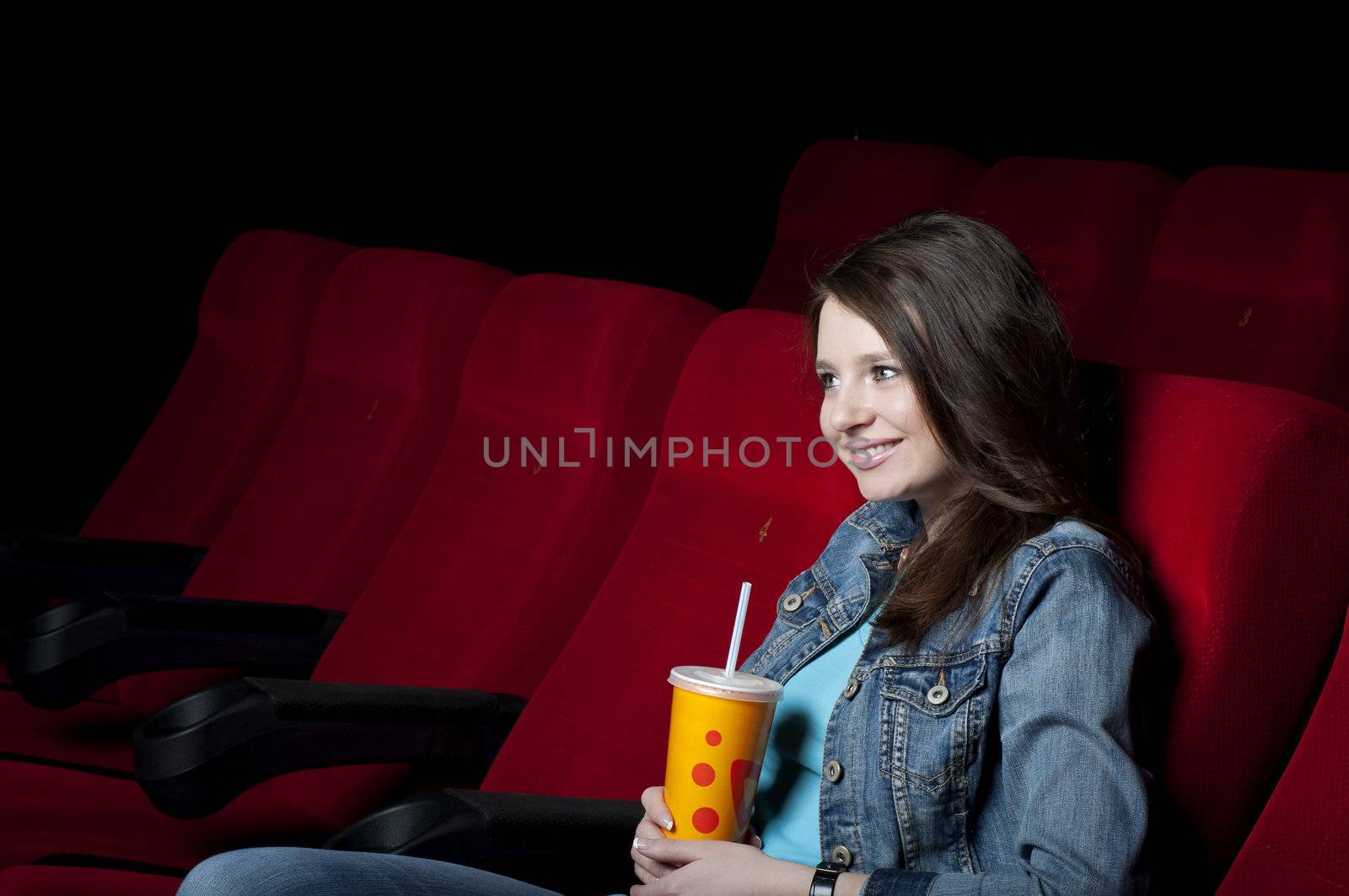 beautiful woman in a movie theater, watching a movie and drink a drink