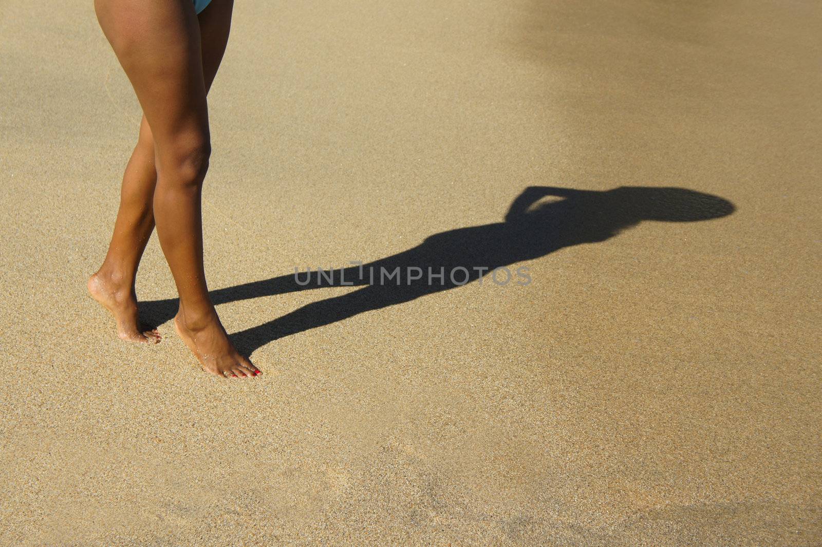 A woman walking on the beach casting a silhouette shadow. 