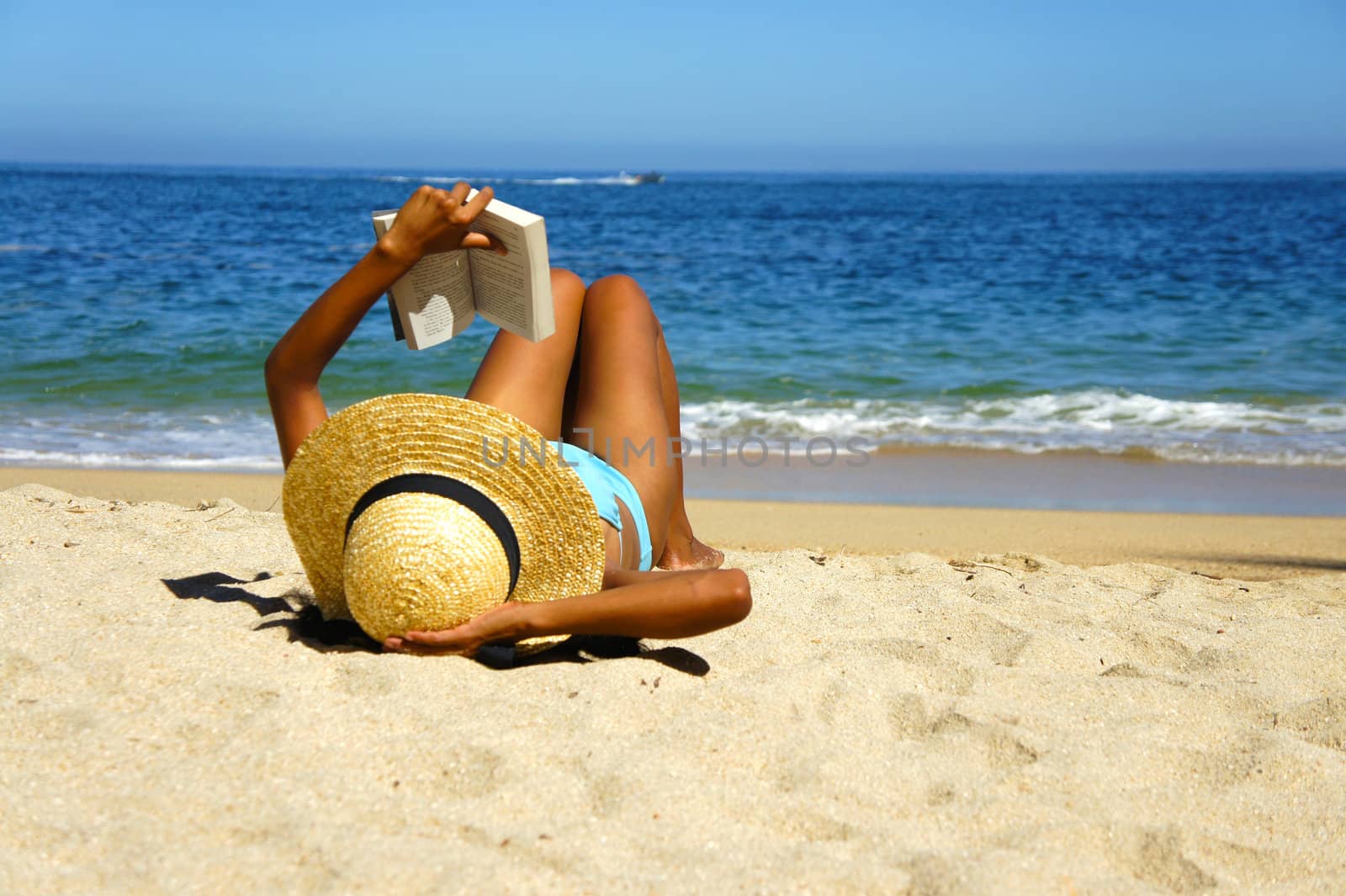A young woman reading a book on the beach. 