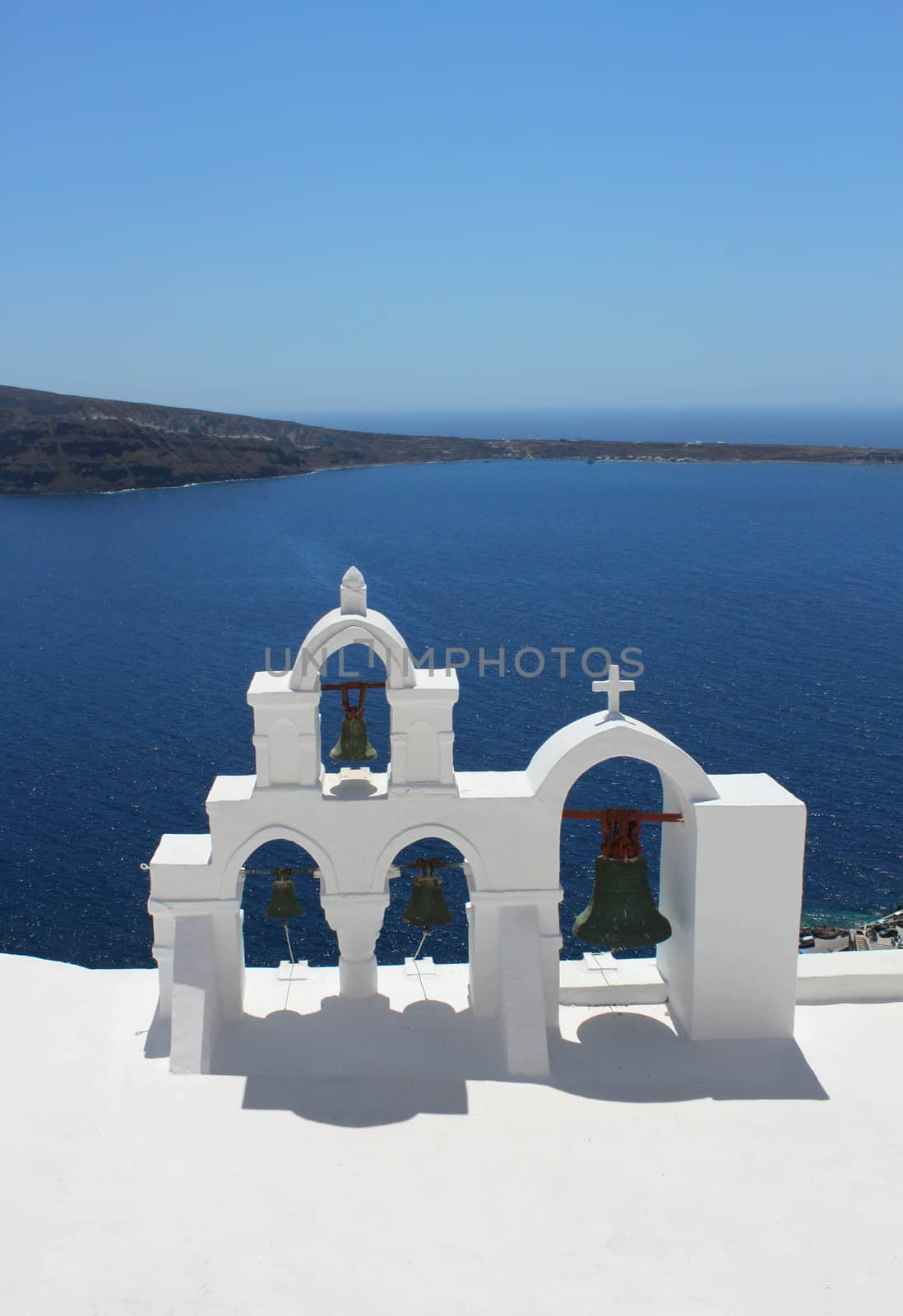 White bell tower of Greek church against blue sea and sky background