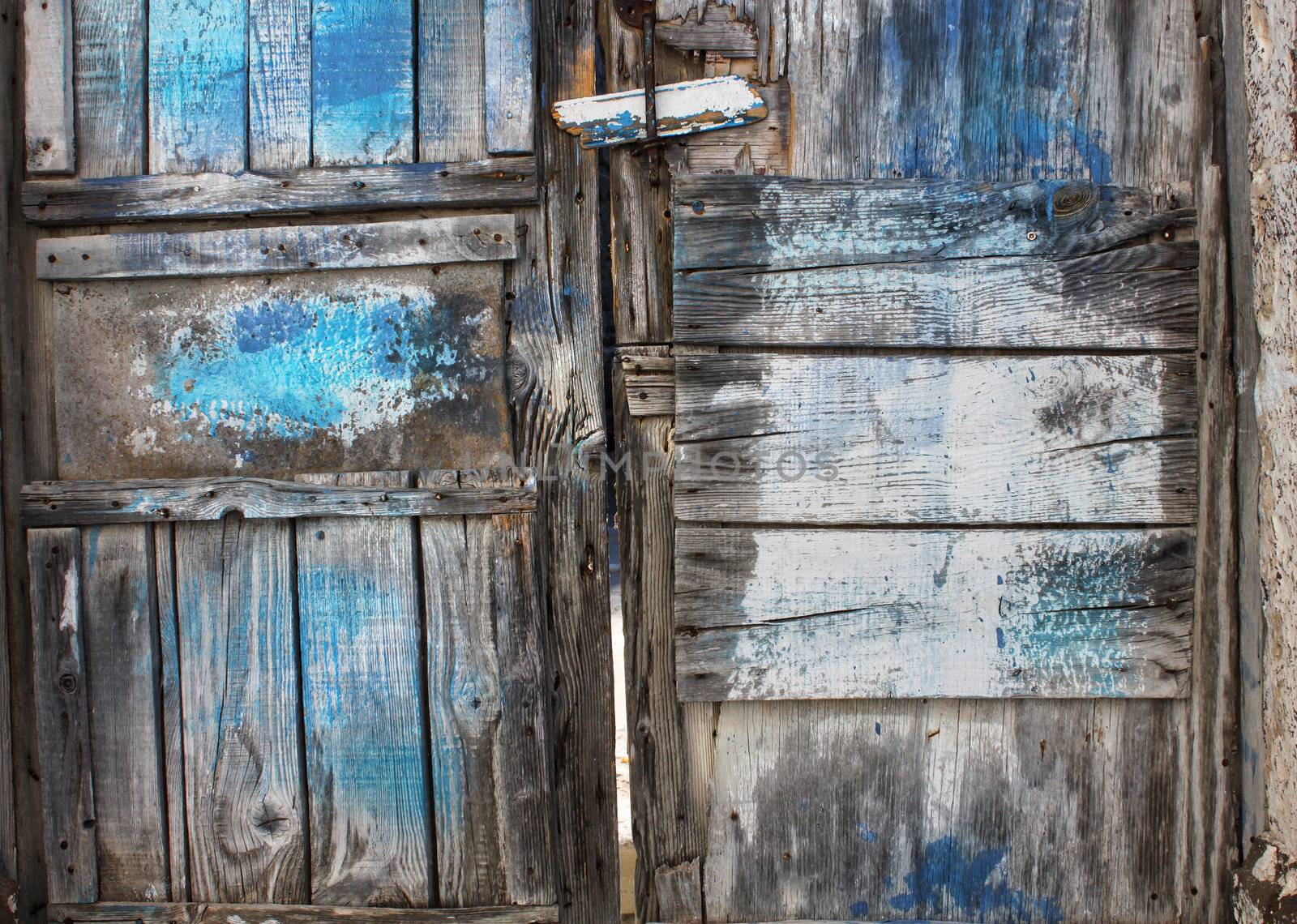 Old rotten wooden door with cracked blue paint stains