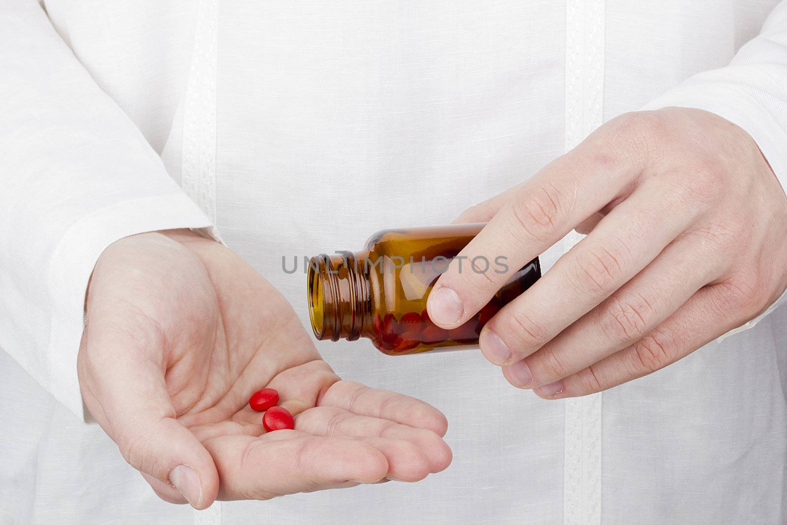 Close-up photograph of a hand pouring red tablets out of a transparent bottle into another hand.