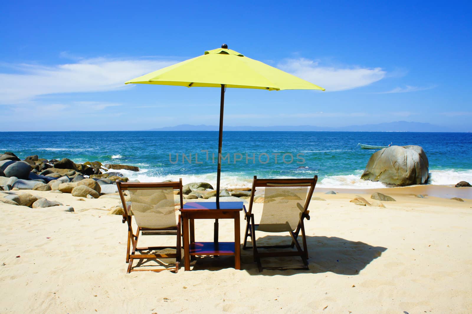 Two chairs a table and a yellow umbrella on the beach