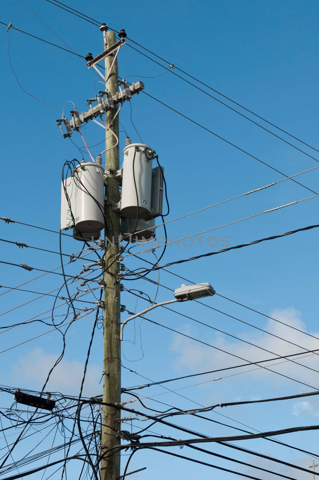 messy old electricity post by the road with power line cables, transformers and phone lines (blue sky background)