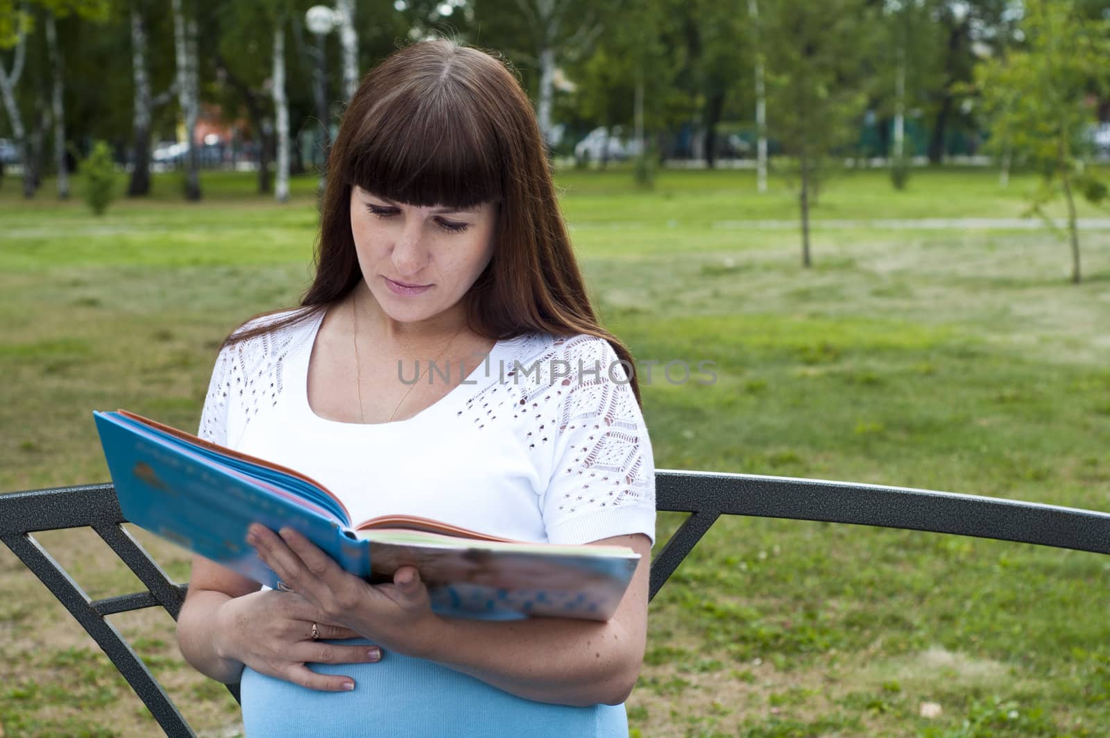 Portrait of nice young smiling woman with book on green background of city park.