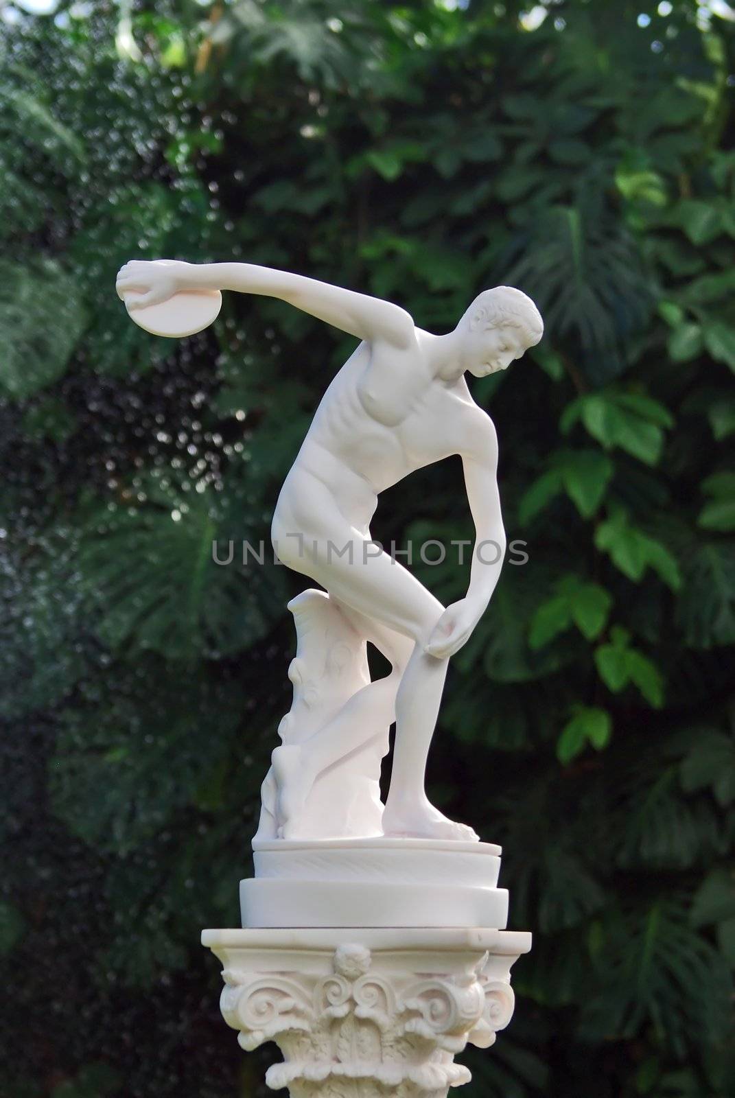 The sculpture of discobolus in park over green leaves