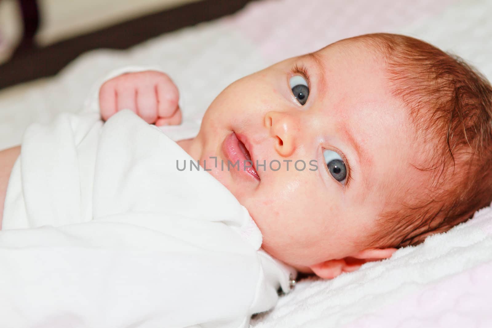 A cute 8 weeks old Caucasian infant smiles as she laying on bed.