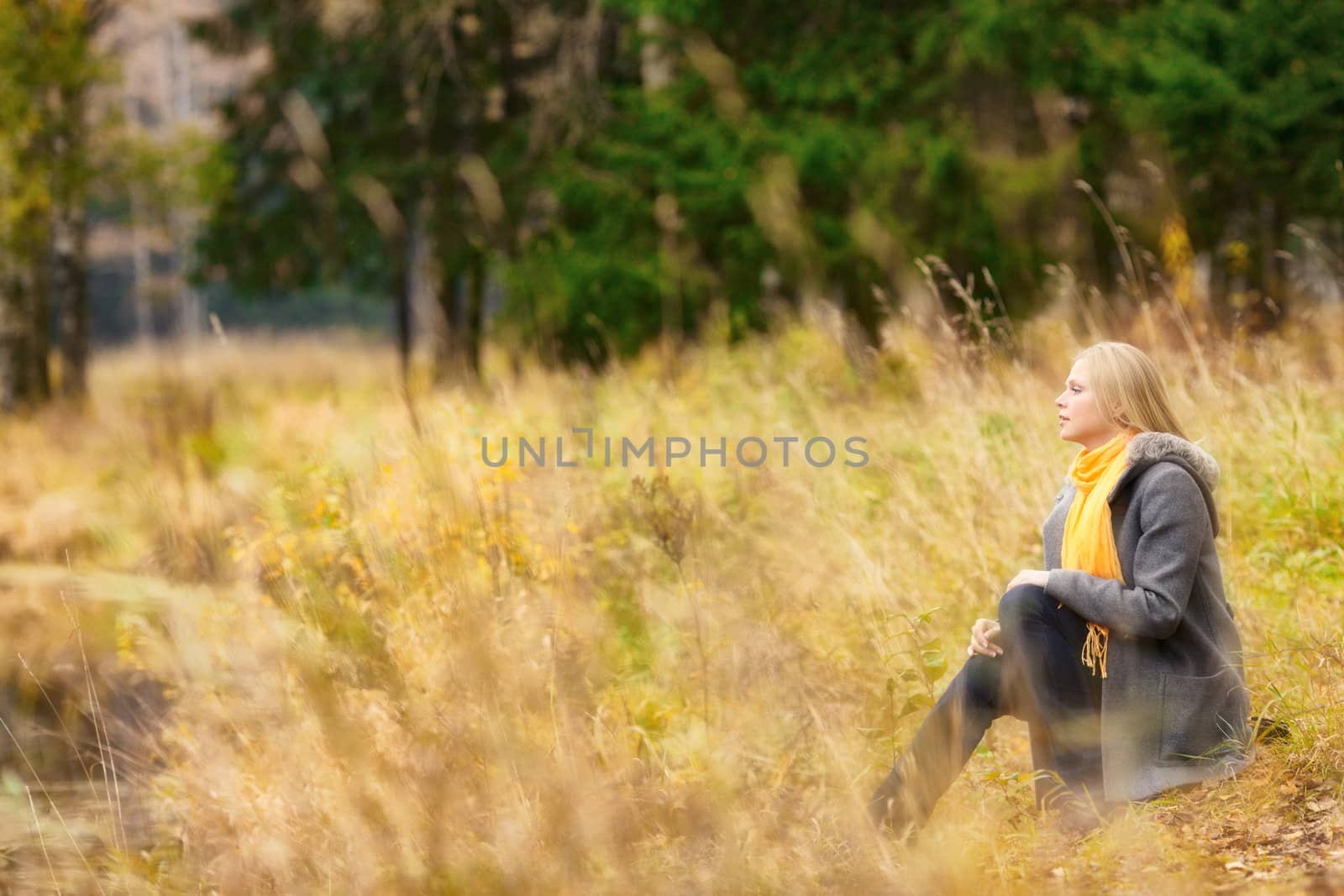 beautiful blond girl sitting on rivershore in autumn forest