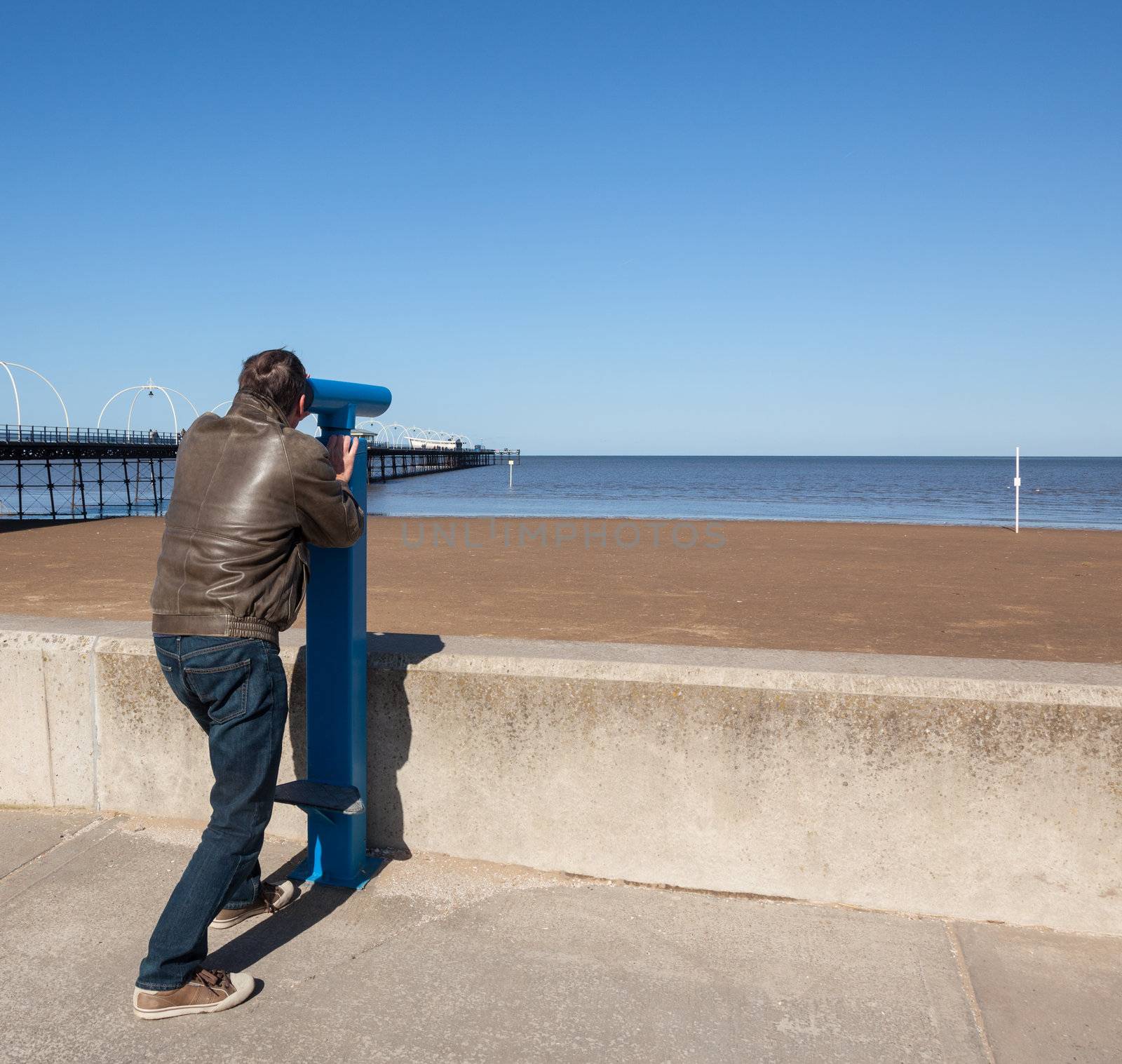 Single caucasian male looking with telescope at sea and pier in Southport England