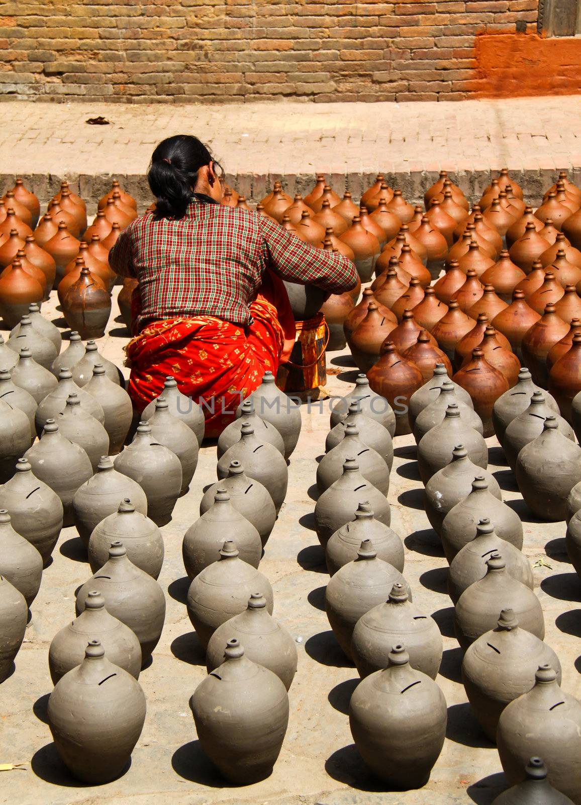 Craftswoman with many clay vases kept for drying