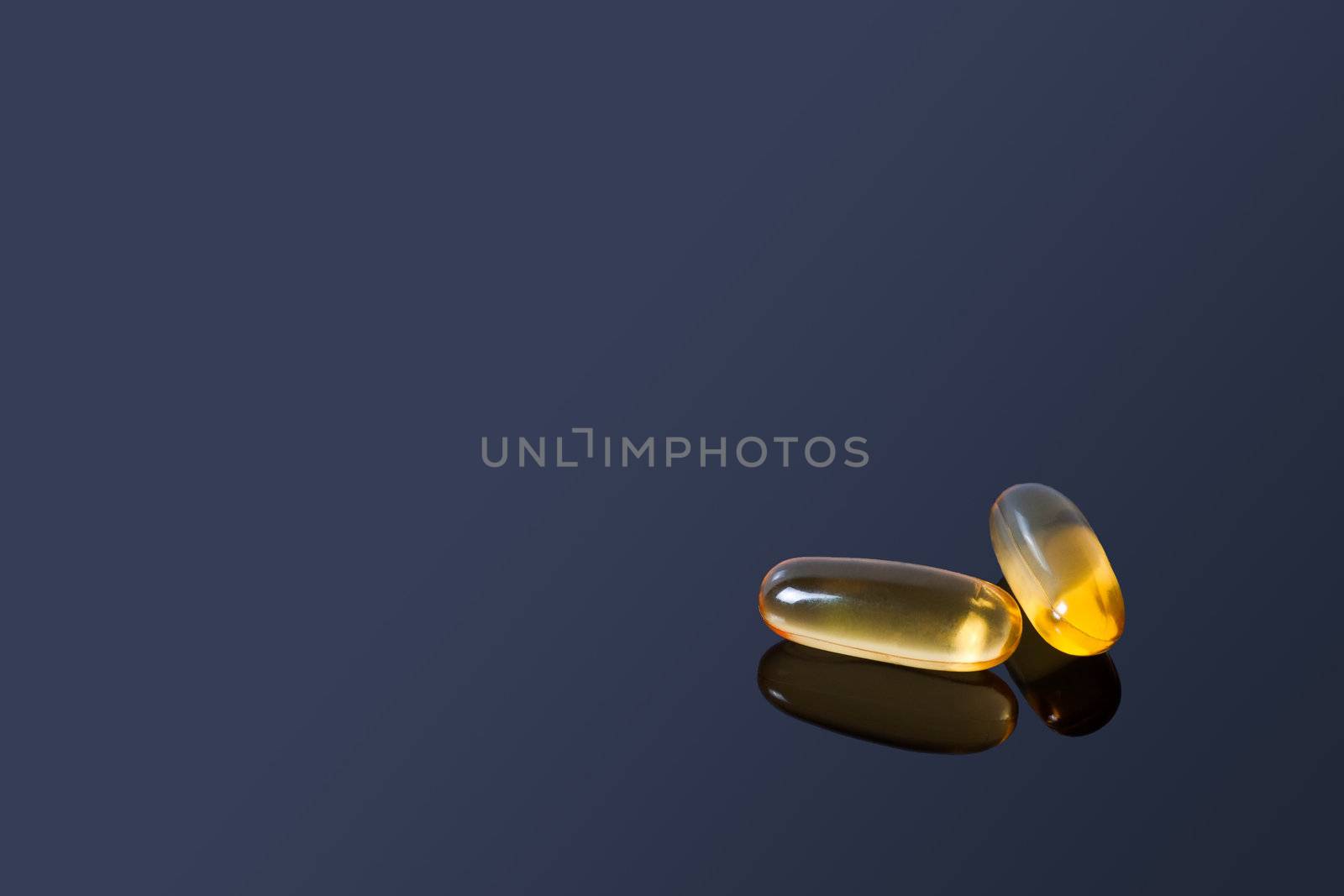 A couple of yellow vitamin pills on a black glass table