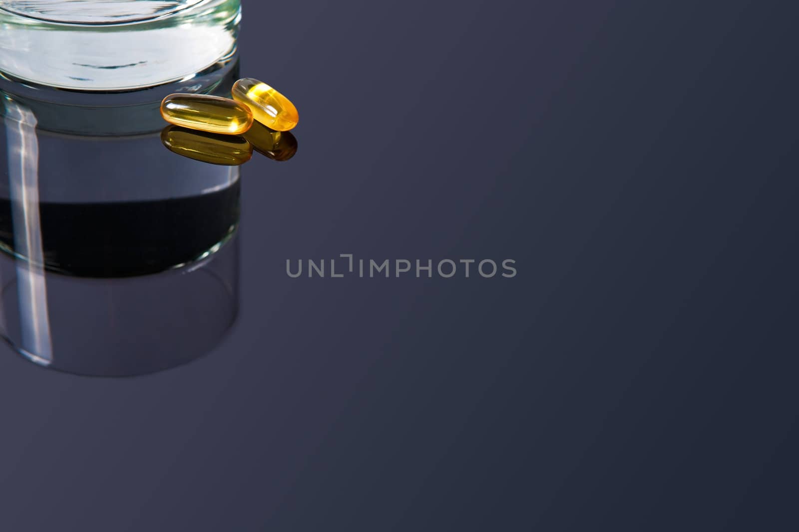 A couple of yellow vitamin pills on a black glass table with a glass of water at the side