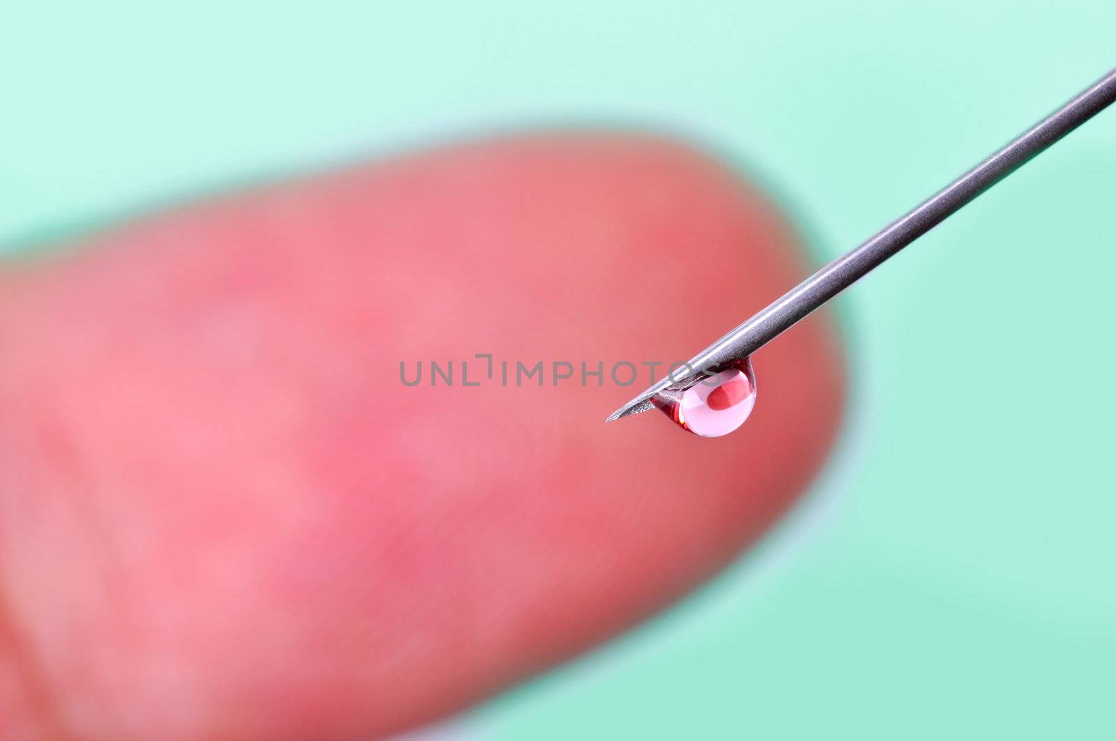 A drop of blood on the tip of a needle and a finger in the background